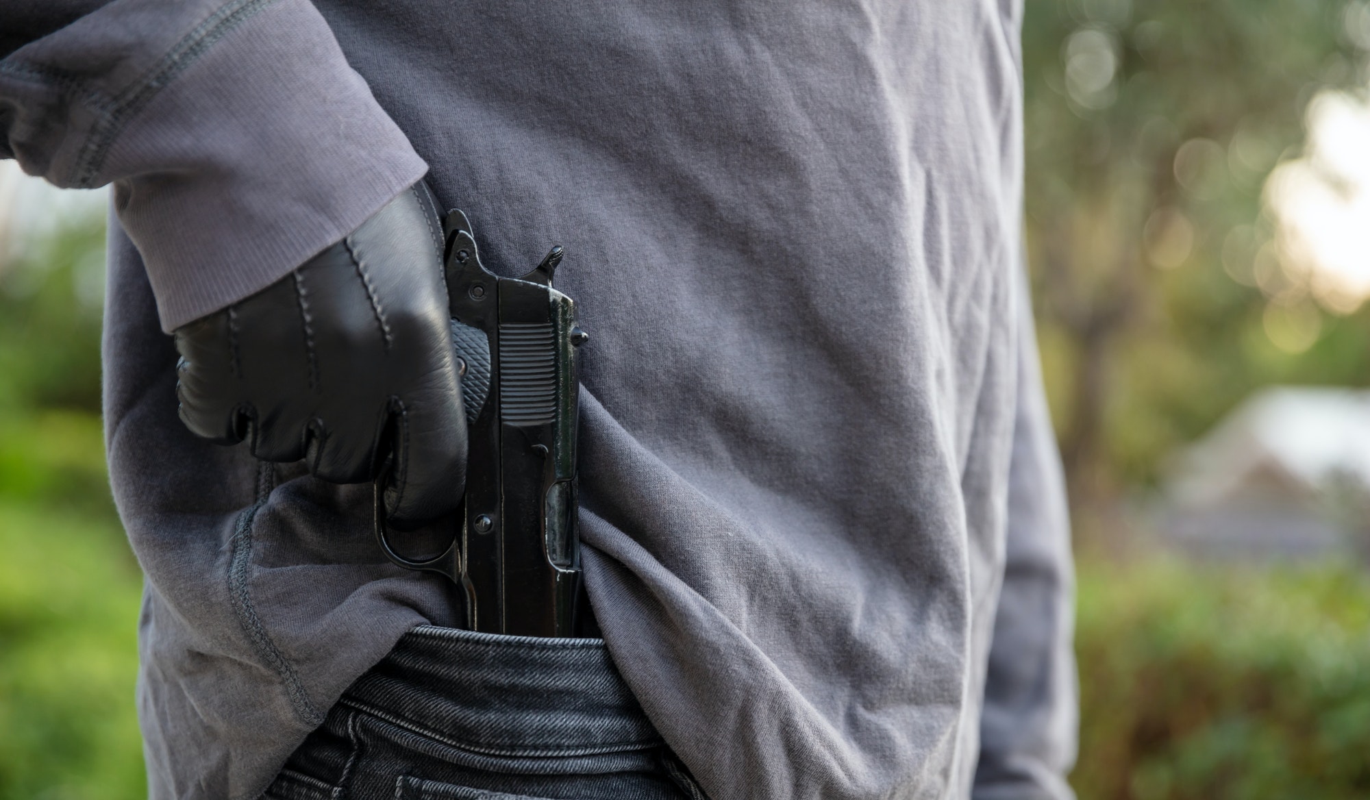 gloved hand holding a pistol blur nature background .jpg